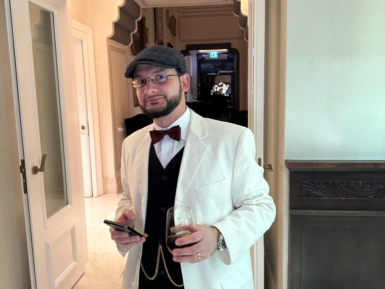 Mario en costume blanc, casquette et nœud papillon, un verre à la main